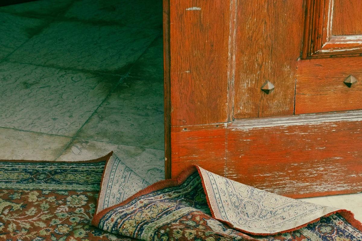 Portuguese rugs, folded on a floor beside a wooden door